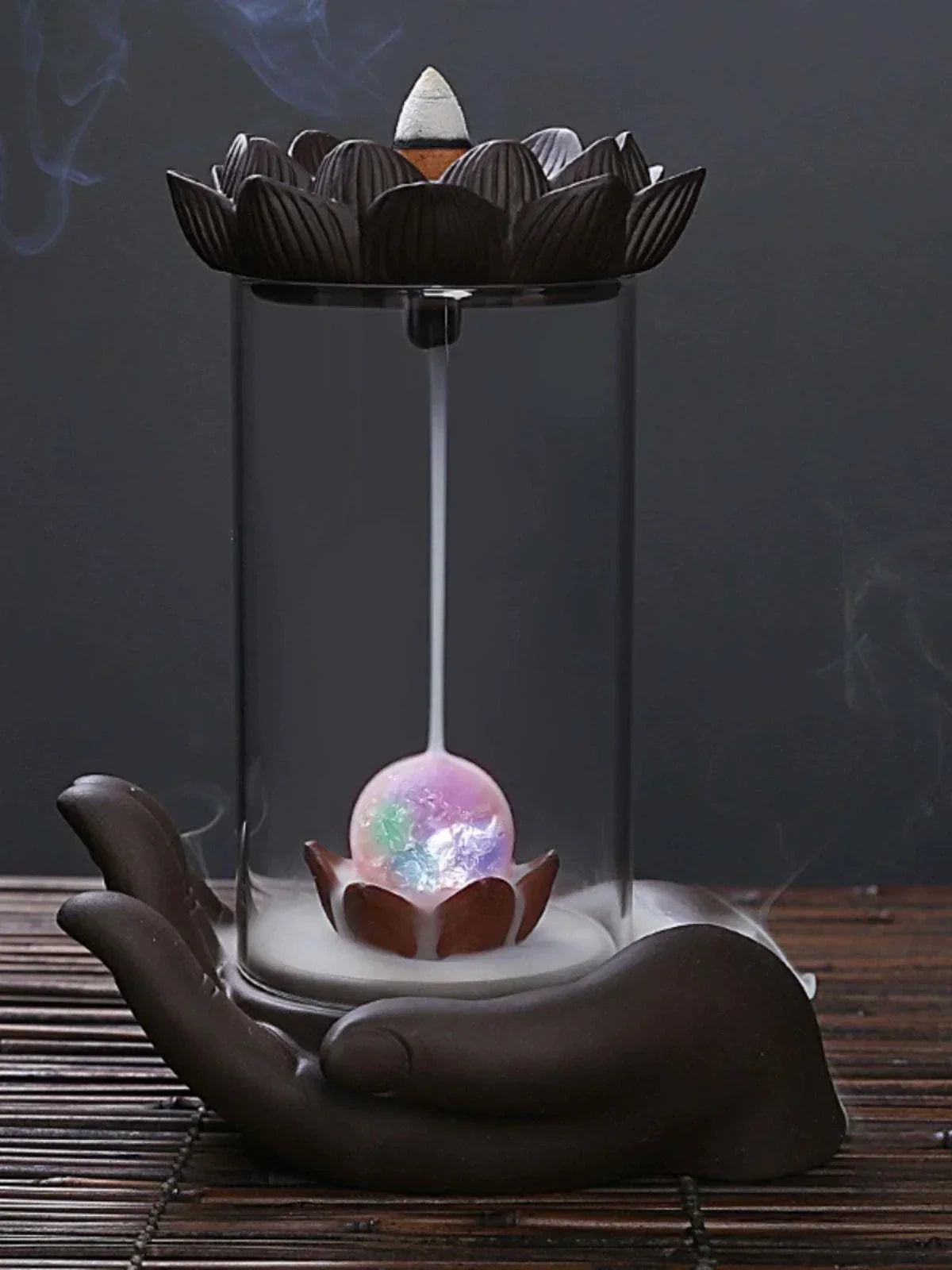 Backflow Purple Sand incense burner with glass lotus and Buddha's hand design releasing smoke cascade in ceramic hand-shaped base.