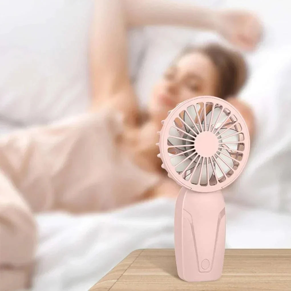 Cute portable handheld pink USB rechargeable fan on wooden table for personal cooling