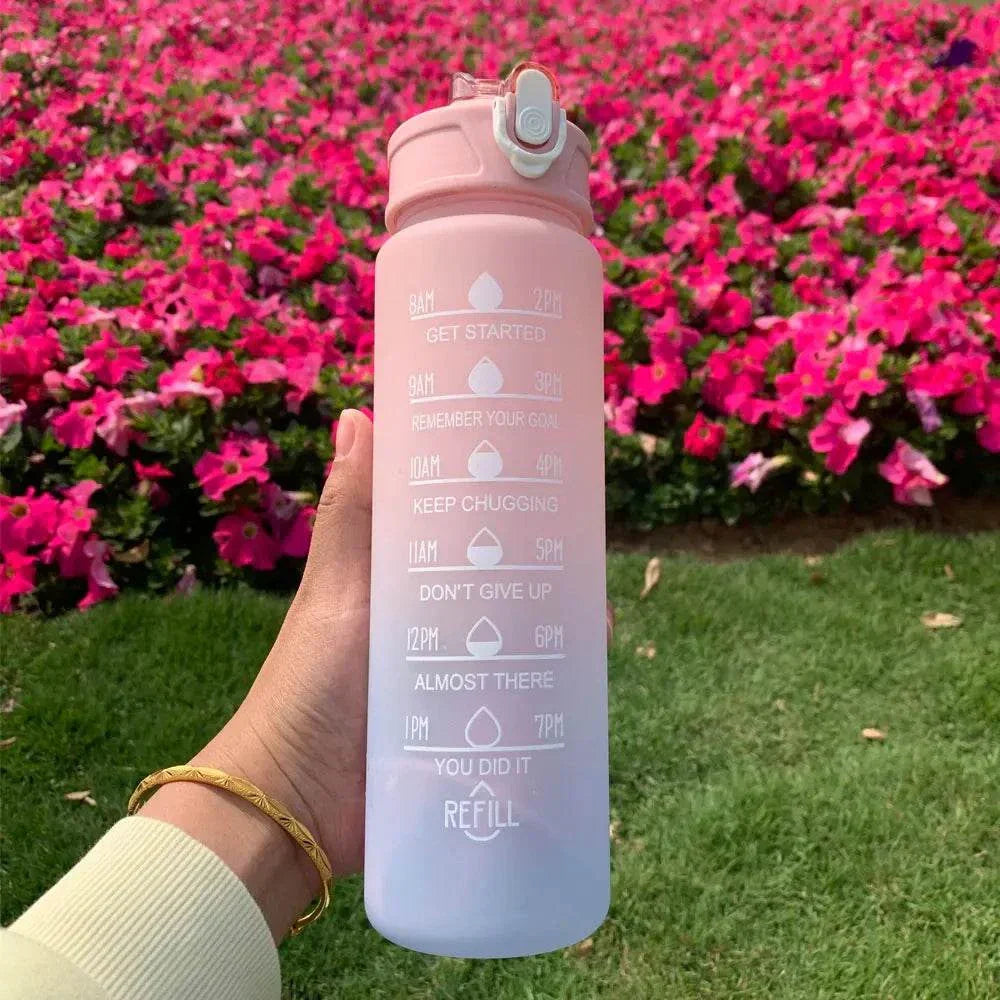 Pink and white gradient water bottle with motivational quotes and time markers held outdoors with pink flowers in the background
