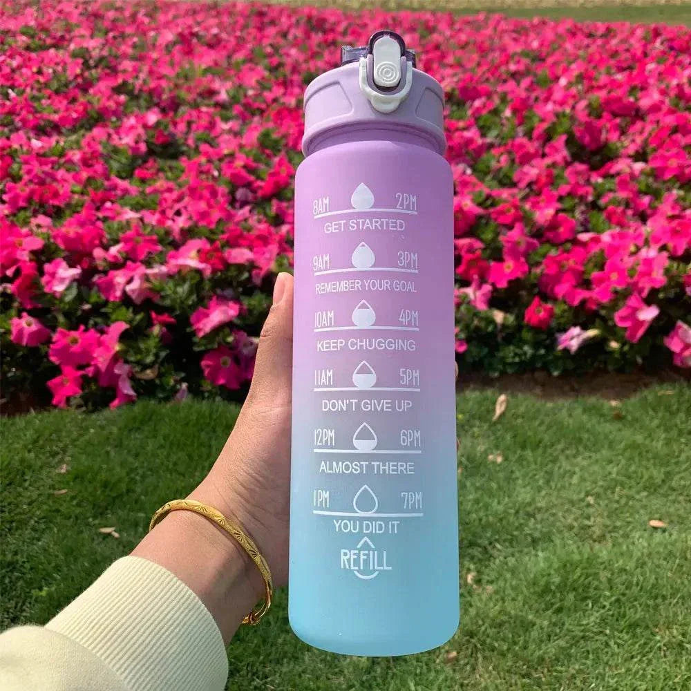 Gradient purple to blue water bottle with motivational quotes and time markers, held outdoors with pink flowers in background
