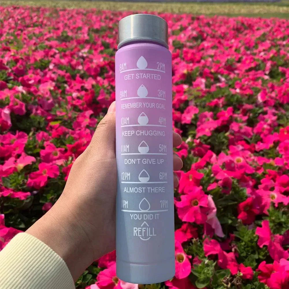 Purple gradient water bottle with motivational quotes and time markers, held in hand outdoors with pink flowers background, reusable sports water bottle with straw